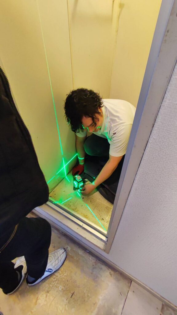 レーザーを使用して浴室ドア枠の建付けを確認している様子