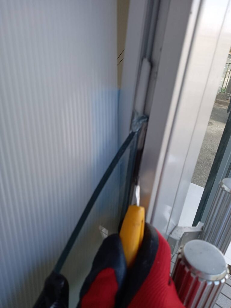 山口市で観音開き店舗ドアの割れたガラスまわりのコーキングを撤去している作業風景